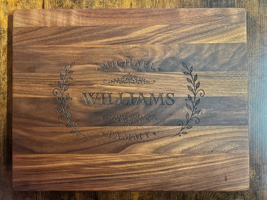 Black walnut cutting board with the Homestead laurel crest engraved across the full face with the names Michael, Tammy and Williams