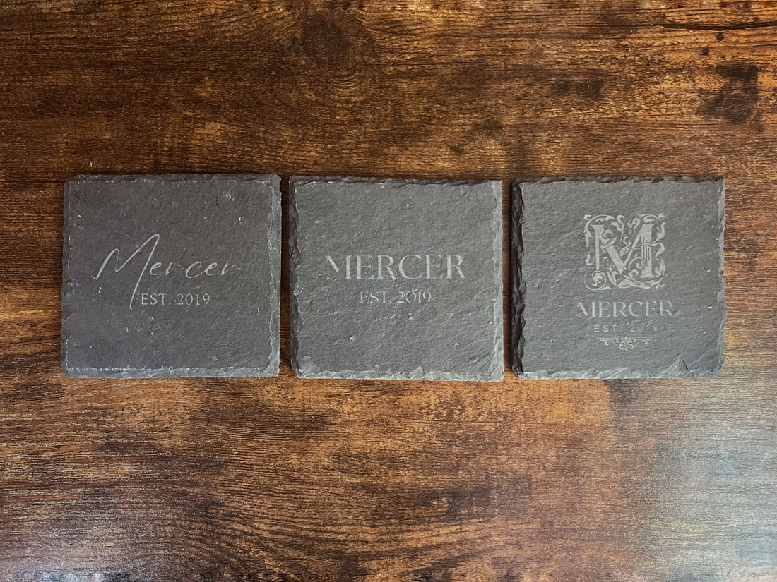 Three engraved slate coasters side by side showing the script, serif and ornate monogram styles