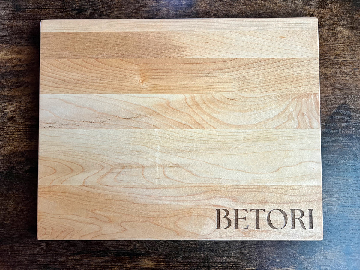 Hard maple cutting board engraved BETORI in serif lettering, shown on a dark wood table