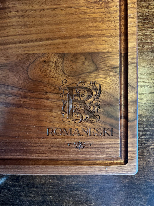 Black walnut cutting board with a juice groove, engraved with an ornate R monogram above the Romaneski family name
