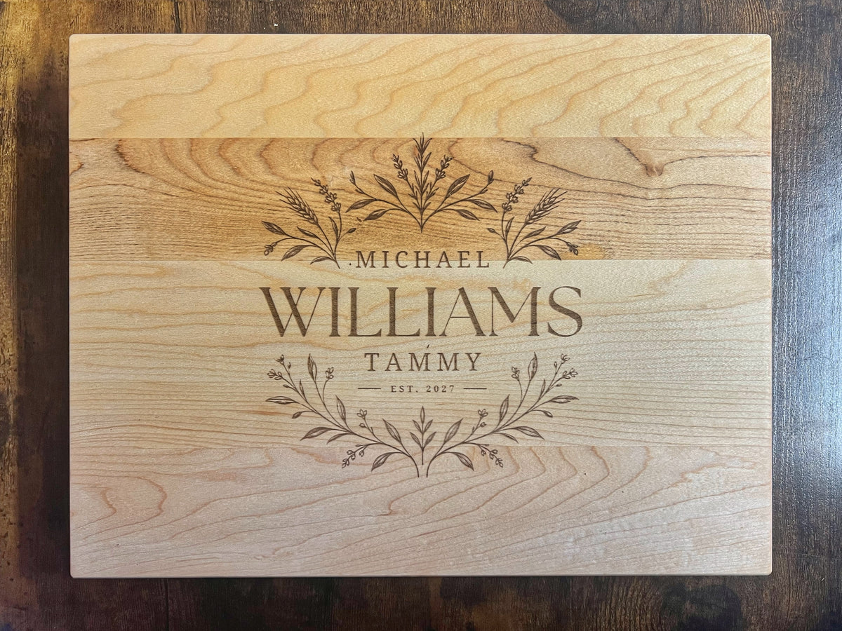 Hard maple cutting board with the Field botanical design engraved across the full face with the names Michael, Tammy and Williams and Est. 2027