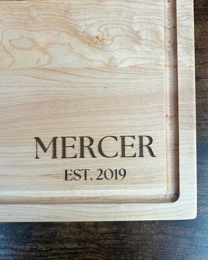 Hard maple cutting board with a juice groove, engraved MERCER EST. 2019 in serif lettering