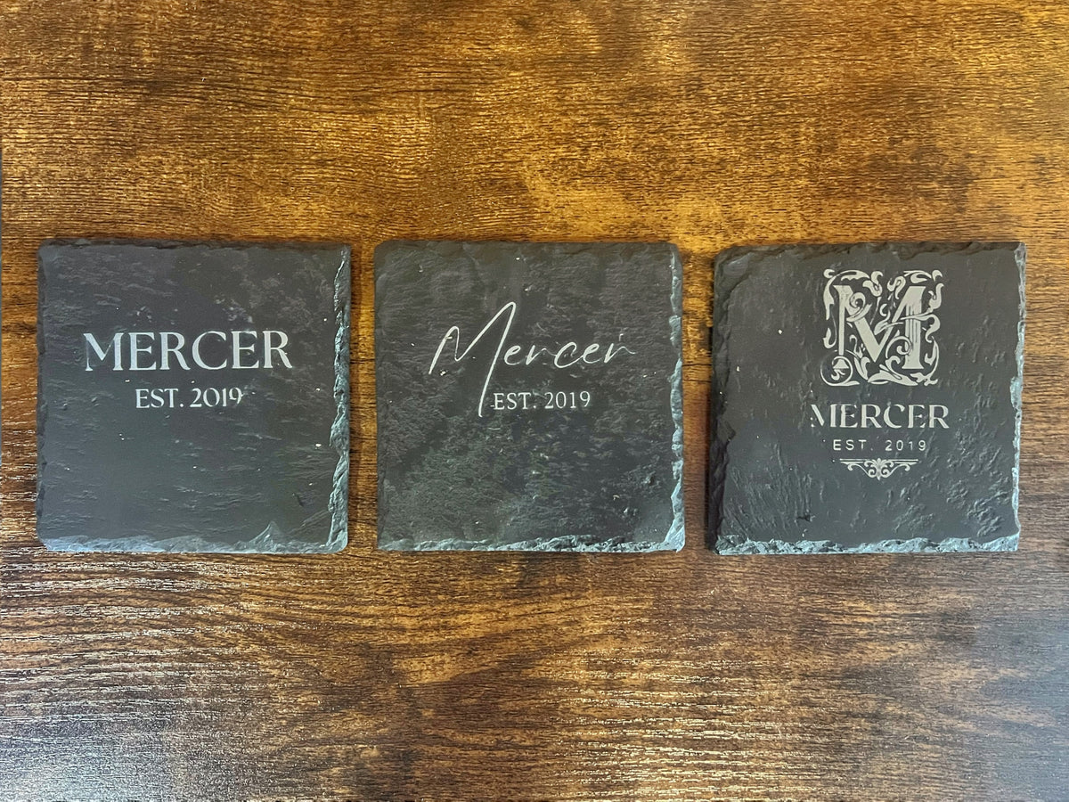 Three engraved slate coasters side by side showing the Serif, Script and Ornate Monogram styles for the Mercer family name