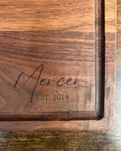Black walnut cutting board with a juice groove, engraved Mercer EST. 2019 in script lettering