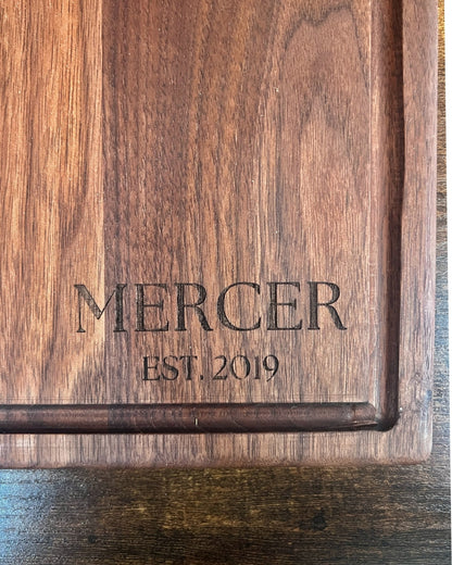 Black walnut cutting board with a juice groove, engraved MERCER EST. 2019 in serif lettering