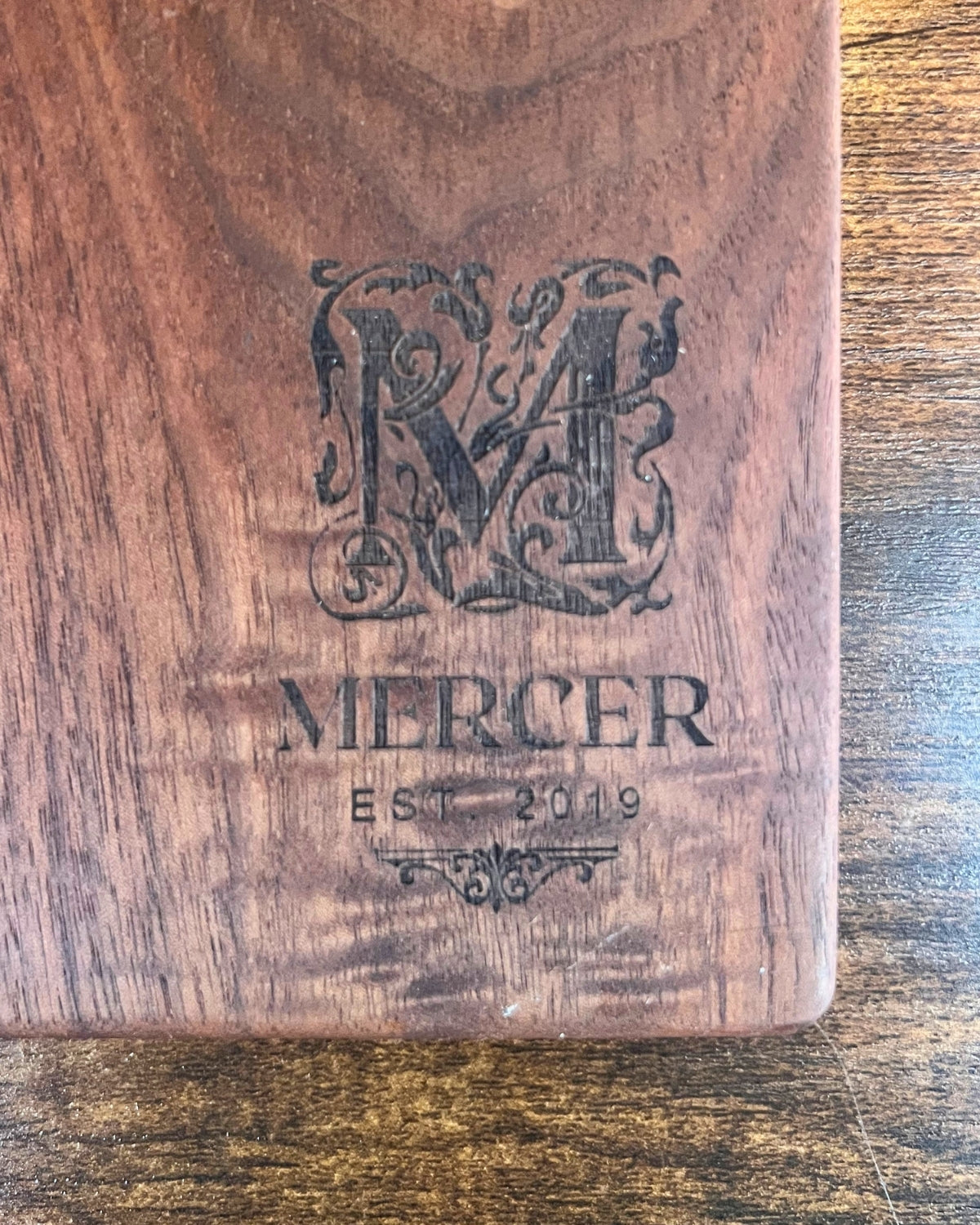 Black walnut cutting board with a smooth finish, engraved with an ornate M monogram above the Mercer family name