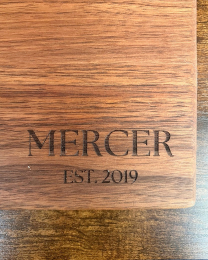 Black walnut cutting board with a smooth finish, engraved MERCER EST. 2019 in serif lettering