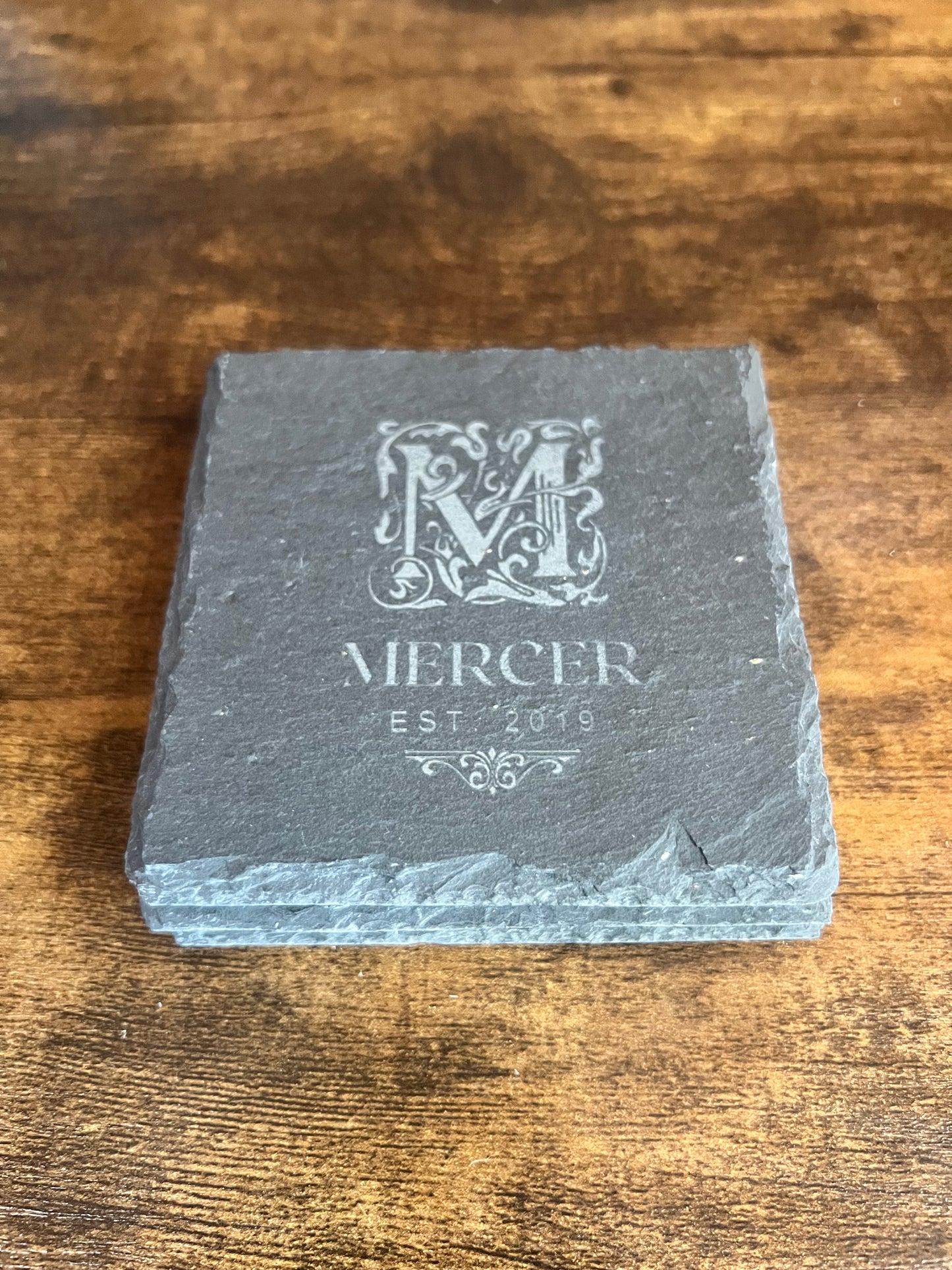 Close view of a slate coaster edge showing the naturally irregular broken stone edge and engraving depth