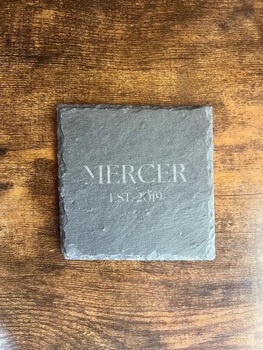Personalized slate coaster engraved MERCER EST. 2019 in serif lettering, shown from above