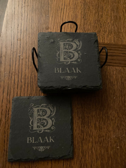 Set of monogrammed slate coasters stacked in a black metal holder on a wood table