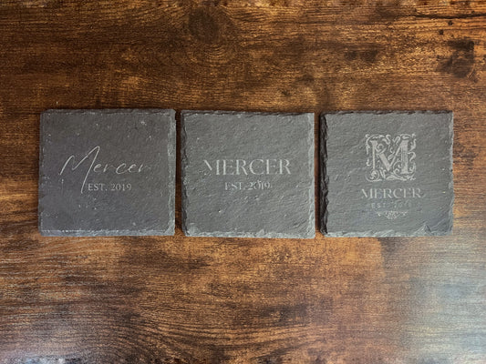 Three engraved slate coasters side by side showing the serif, script and ornate monogram styles