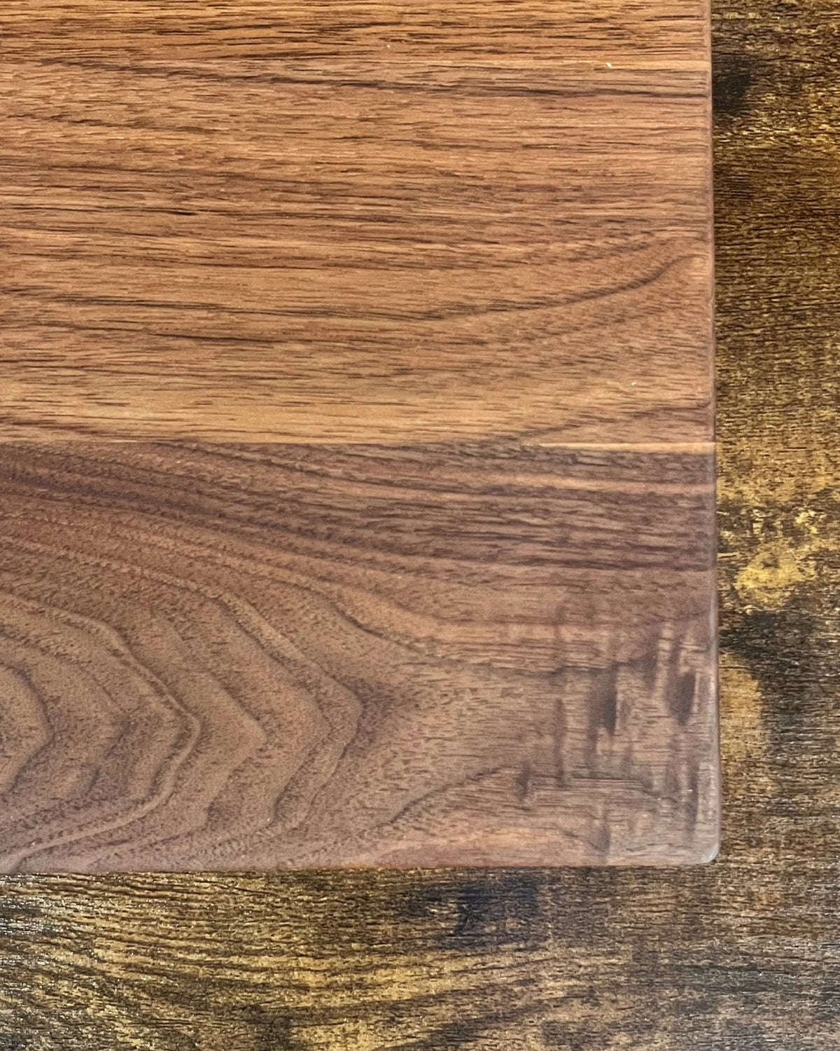 Black walnut cutting board with a smooth finish and no engraving, showing the natural grain and rounded edge